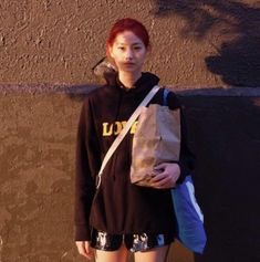 a woman with red hair is holding a brown bag and standing in front of a wall