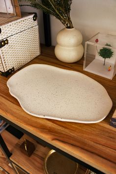 a white vase sitting on top of a wooden table next to a plant and other items