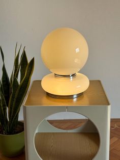 a white table lamp sitting on top of a wooden stand next to a potted plant