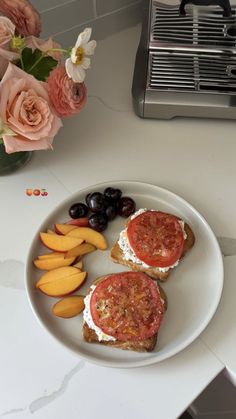 two sandwiches with tomatoes, cheese and fruit on a plate next to a vase of flowers