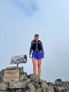 a woman standing on top of a pile of rocks next to a sign and backpack