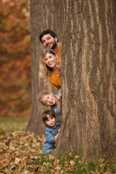 a man and two children standing next to each other near a tree with leaves on the ground