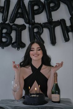 a woman sitting in front of a cake with candles on it and a bottle of wine next to her