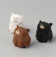 three small plastic animals sitting next to each other on a gray surface with one black bear, one white bear and one brown bear