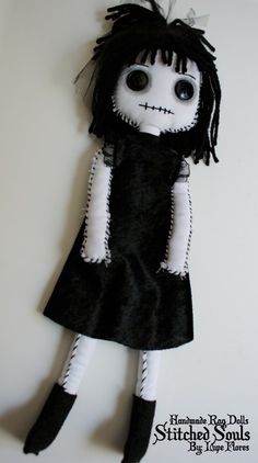 a black and white stuffed doll with long hair wearing a black dress on top of a wall