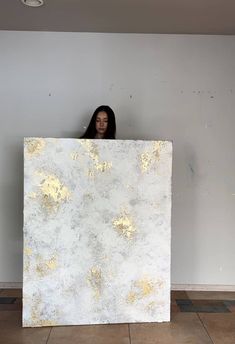 a woman standing behind a large piece of white and gold paint on the wall in an empty room