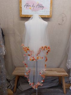 a white veil with orange and pink flowers hanging from it's side on a wooden bench