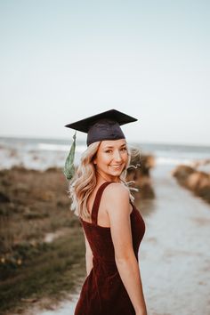 a woman wearing a graduation cap and gown in front of the ocean with her hair blowing in the wind