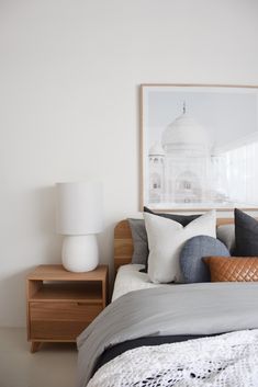 a bed with grey and white pillows on top of it next to a wooden night stand