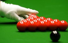 a pool table with several red balls on it and a hand reaching for the ball