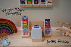 a wooden table topped with toys and boxes filled with books next to a rainbow wall