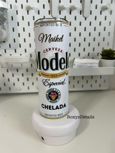 a can of model beer sitting on top of a white table next to a potted plant