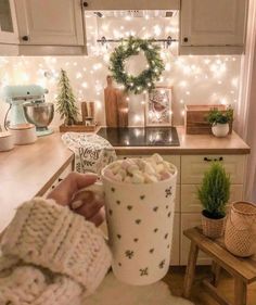 a person holding a cup filled with marshmallows in front of a kitchen counter