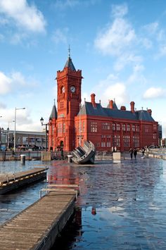 a large red building with a clock on it's tower next to a body of water