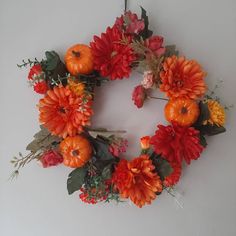 a wreath made out of flowers and pumpkins hanging on the side of a wall