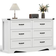 a white dresser with drawers and a lamp next to it on top of a table