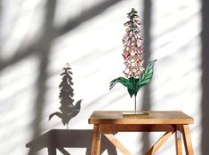 a wooden table topped with a flower next to a shadow of a tree on the wall