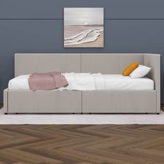 a bed sitting on top of a hard wood floor next to a wall mounted painting