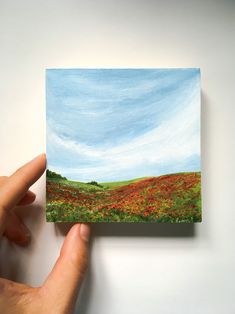 a hand holding up a small piece of paper that is painted with flowers on it