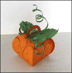 an origami heart shaped box with green leaves on the top and ribbon tied around it