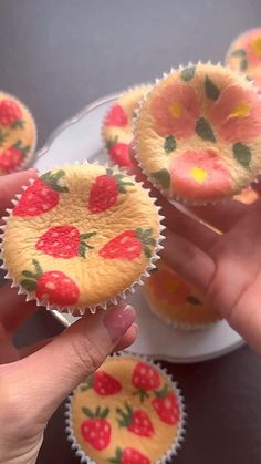 cupcakes with strawberries painted on them being held by someone