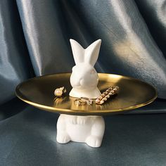 a white rabbit figurine sitting on top of a gold platter with beads