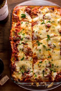 a casserole dish with meat and cheese on it next to a bottle of wine