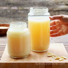 two jars filled with yellow liquid sitting on top of a wooden table next to bowls