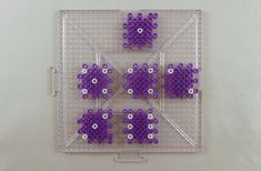 four purple and white beads are arranged in the shape of an x on a clear tray