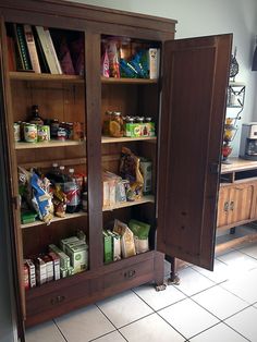 an open cabinet with food in it on the floor next to a counter and cabinets