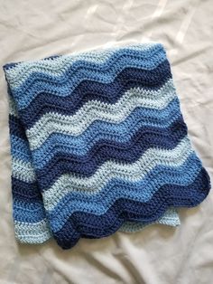 a blue and white crocheted blanket laying on top of a bed next to a pillow