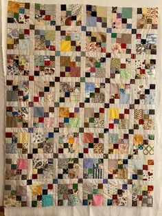 an old quilt hanging on the wall in front of a white curtain with many different colored squares