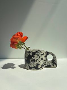 a vase with a flower in it sitting on a table next to a white wall