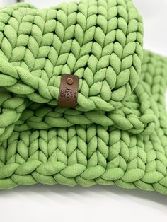 two green knitted blankets folded on top of each other with a brown tag in the middle