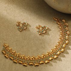 a gold necklace and earring set with turquoise stones on a table next to a bowl