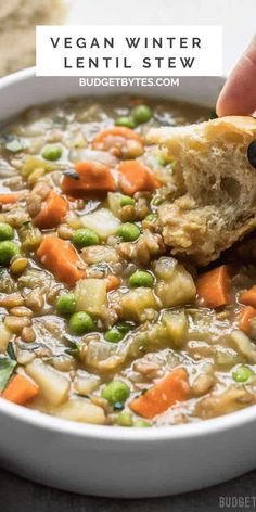 a person dipping a piece of bread into a bowl of vegetable soup with peas and carrots