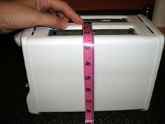 a person is measuring the width of a toaster with a pink tape on it