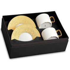 a black box with three white and gold plates in it, two cups and one saucer