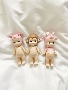 three little dolls sitting next to each other on a white sheet in the shape of monkeys