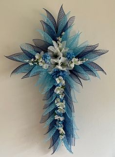 a cross made out of blue and white flowers with feathers on the side, attached to a wall