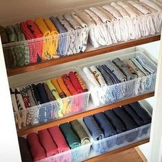 the closet is full of folded shirts and other items in plastic bins on wooden shelves