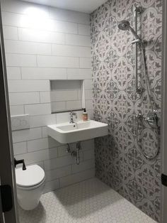 a white toilet sitting next to a sink in a bathroom under a shower head mounted on a wall