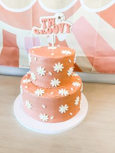 a three tiered cake with pink frosting and white daisies on the top