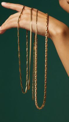 a woman's hand holding several gold chain bracelets