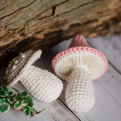 two crocheted mushrooms sitting on top of a wooden table next to a plant