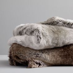 two fur pillows sitting on top of each other in front of a gray wall and floor