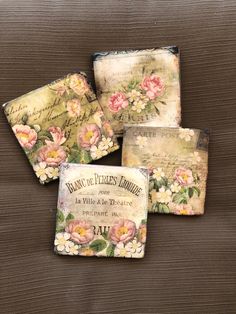 four coasters with flowers on them are sitting on a wooden surface, one has writing and the other has french script