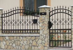 an iron gate and stone wall in front of a house