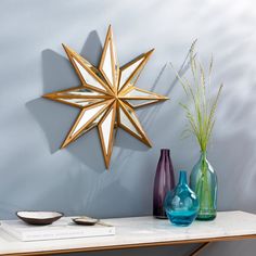 two vases and a star shaped mirror on a table in front of a wall