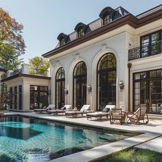 a house with a swimming pool and lounge chairs in front of the home's large windows